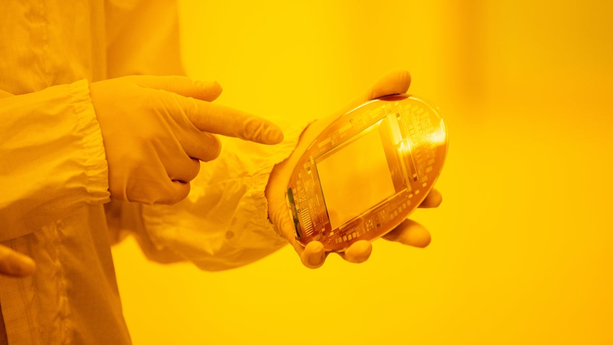 Person in lab equipment and gloves pointing at a device they are holding