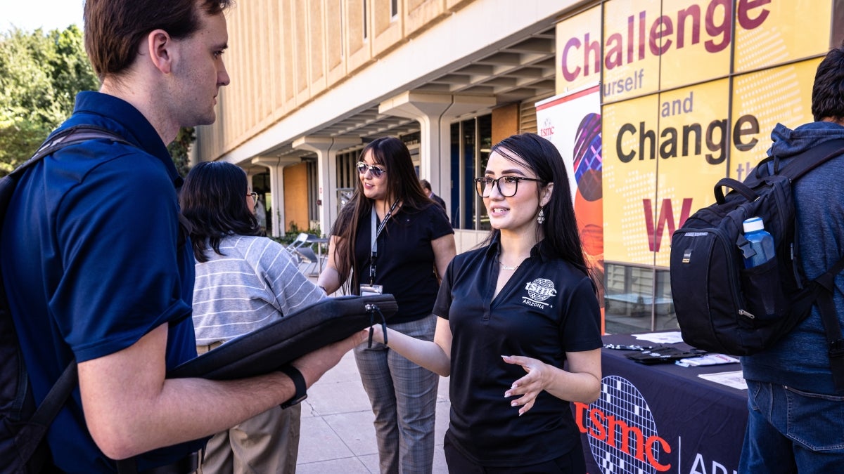 Person with blue TSMC shirt and glasses demonstrating to another person at a vendor booth