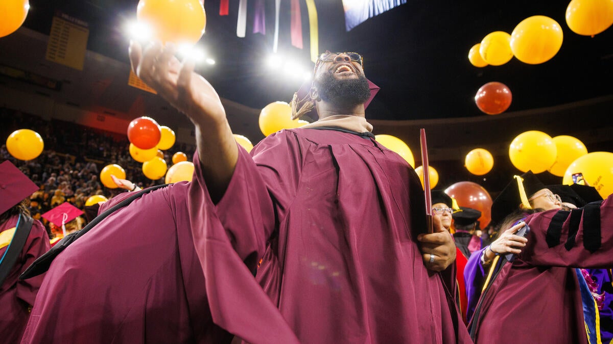 Students celebrating at commencement with gold and maroon balloons