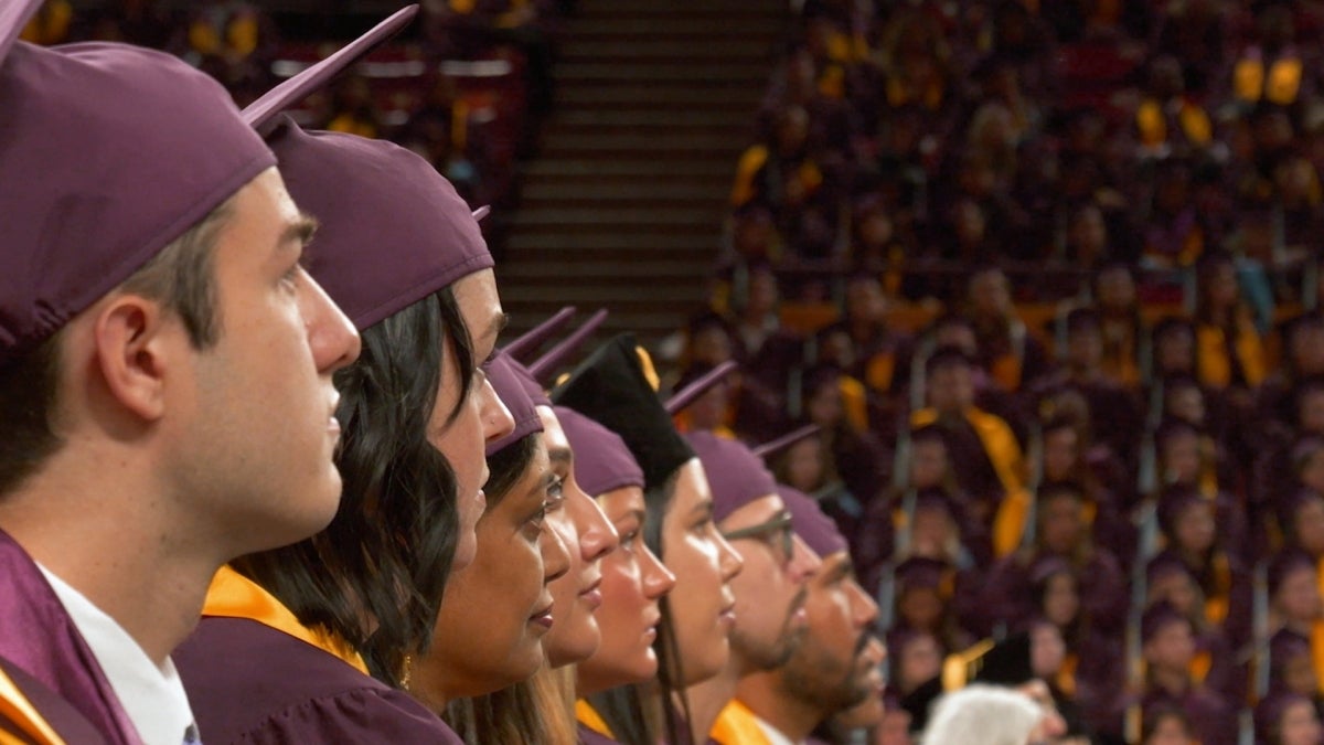 Arizona State University graduates in robes and caps listen to a speaker at Desert Financial Arena